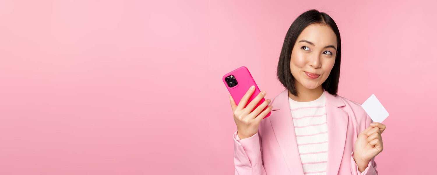 Smiling Asian Corporate Woman Lady Suit Thinking Holding Smartphone Credit Card Plan Buy Smth Online Shopping With Mobile Phone Pink Background 2